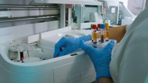 Gloved hands loading blood samples into a laboratory analyser