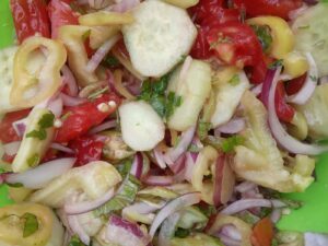 A bowl of fresh vegetables sits beside a small dish of golden olive oil.